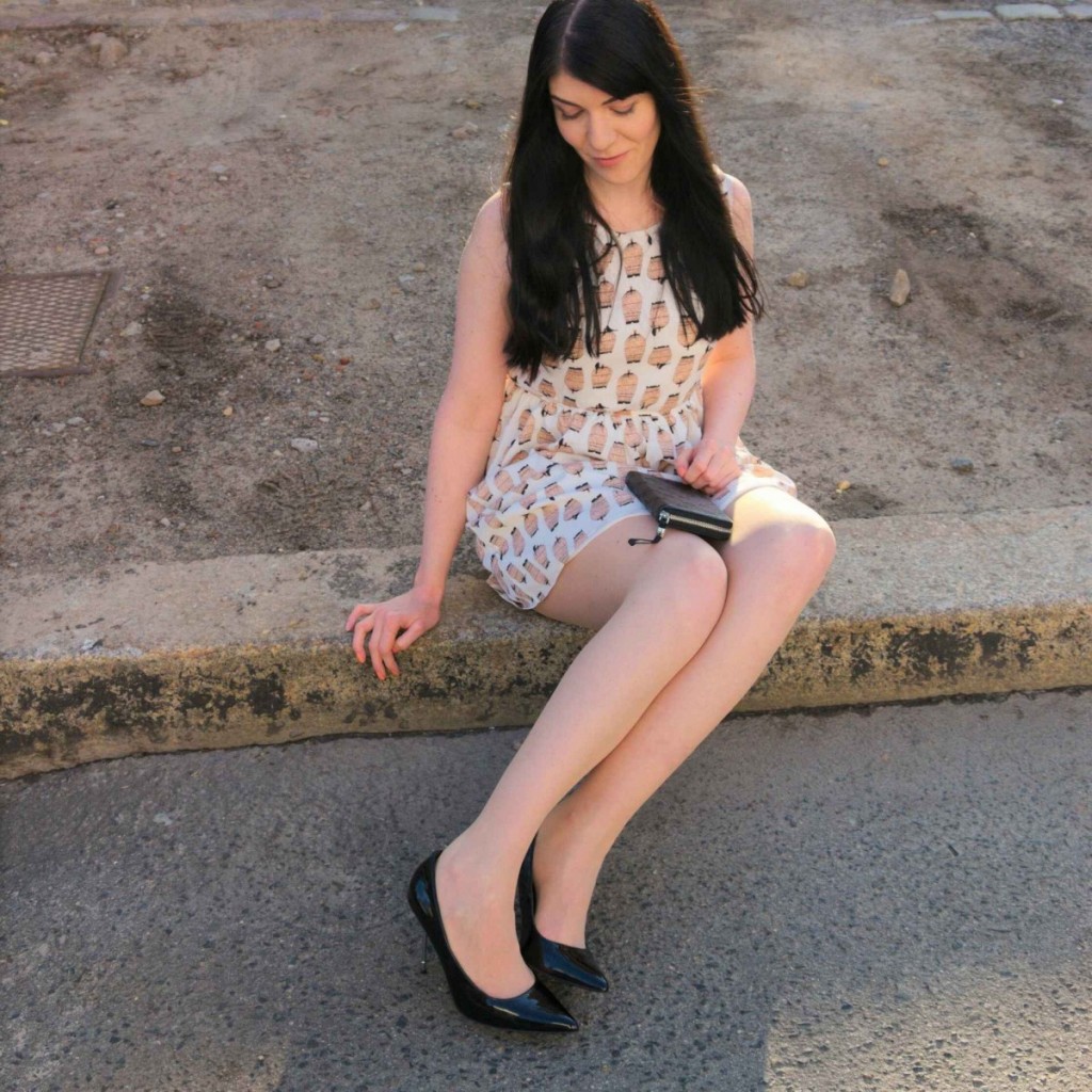 Brunette in Birdcage print pastel dress and metal stiletto high heels sitting at the curb