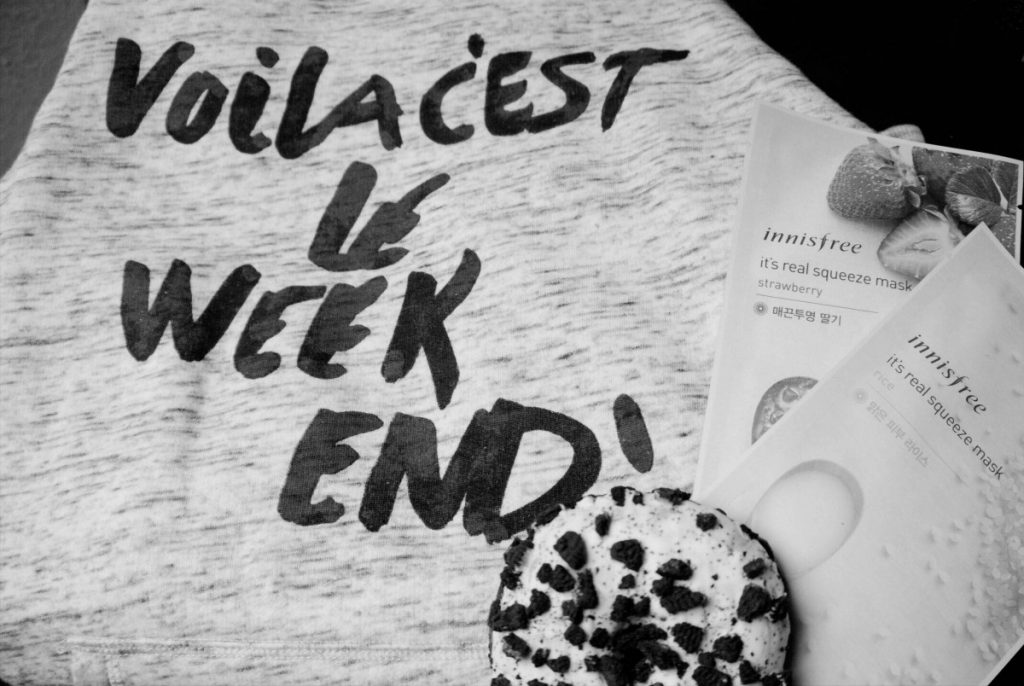 black and white image of sweater with voila c'est le weekend print, oreo donut and korean sheet masks by Innisfree in a flatlay